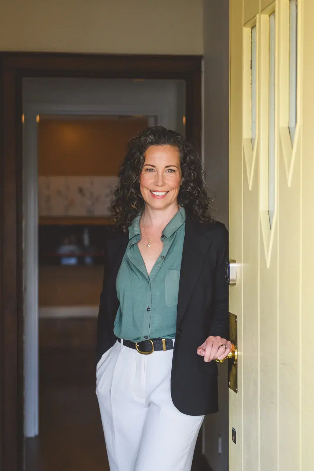 Heather Young stands at the open front door of her St. Agatha office in a green blouse and navy blazer, smiling warmly.