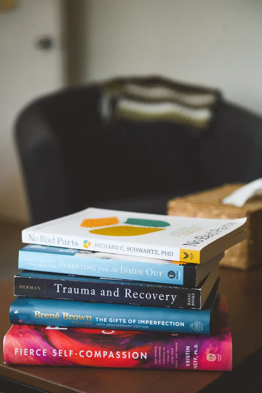 A stack of therapy books on the coffee table: No Bad Parts, Parenting from the Inside Out, Trauma and Recovery, The Gifts of Imperfection, Fierce Self-Compassion.