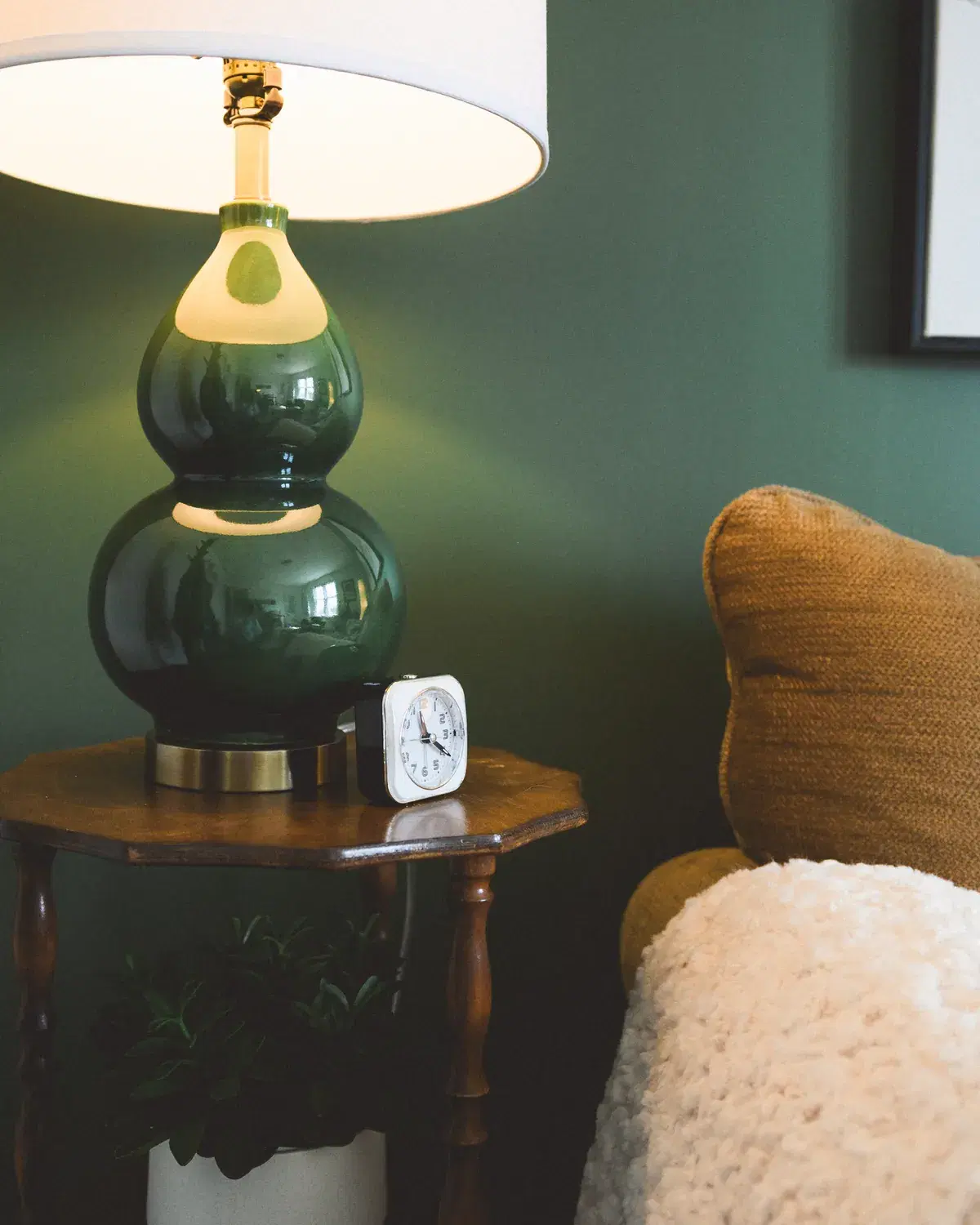 A warm table lamp beside an armchair in a quiet counselling room, its glow soft against a deep green wall.